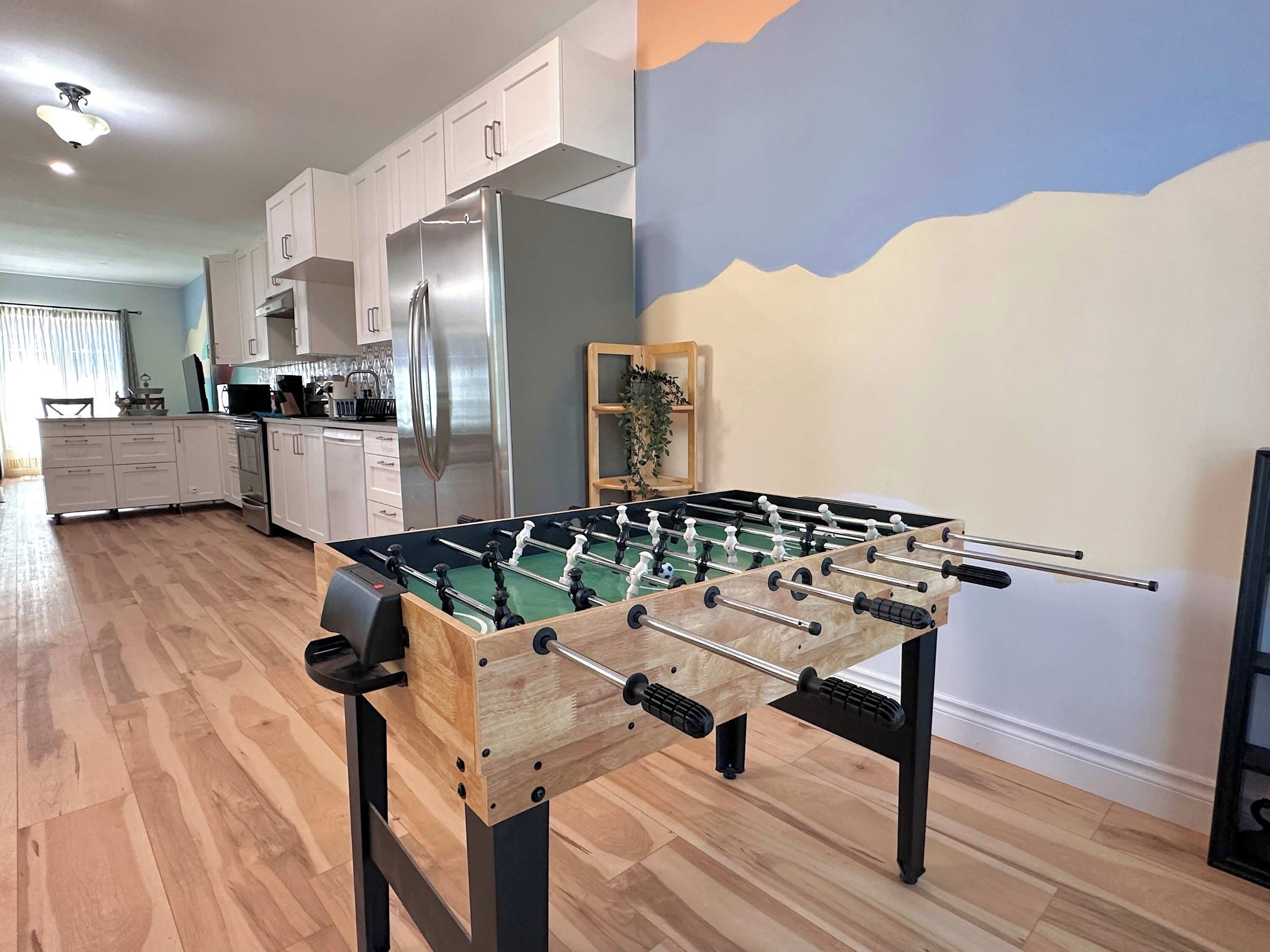 A modern kitchen with a foosball table, stainless steel appliances, and a view of the outdoors.