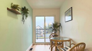 Ein Zimmer mit Glastür und Zugang zu einem Balkon, Korbmöbeln und Topfpflanzen.
