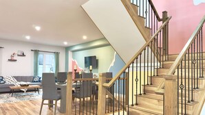 A modern living room with a wooden staircase, a dining area, and a sofa. - Lake Erie Blue Room Getaway (Port Colborne)
