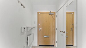 A hallway with a wooden door, a mirror, a light switch, and a thermostat. - Nordic Abode in Central Reading - Balcony (Reading)