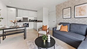 A modern living room with a grey sofa, a dining table with chairs, a kitchen in the background, and artwork on the wall. - Nordic Abode in Central Reading - Balcony (Reading)