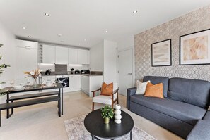 A modern living room with a grey sofa, a dining table with chairs, a kitchen in the background, and artwork on the wall. - Nordic Abode in Central Reading - Balcony (Reading)
