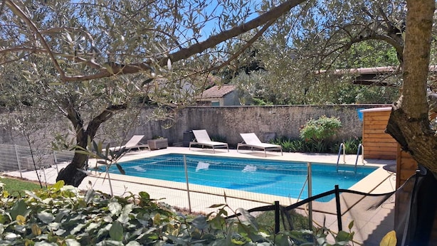 Una piscina con sillas de descanso, rodeada de vegetación y un muro de piedra.