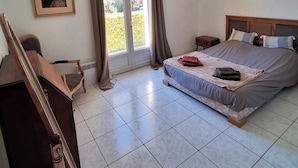 Un dormitorio con cama, escritorio, silla, marco de foto y ventana con cortinas.