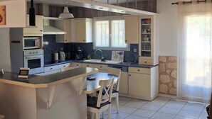 Una cocina con isla central, horno empotrado y comedor con sillas.