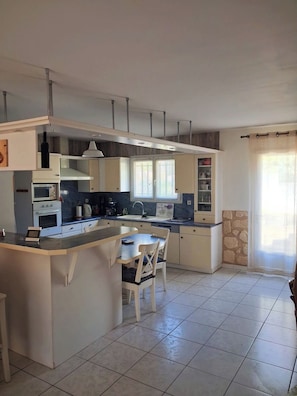 A kitchen with a central island, built-in oven, and a dining area with chairs. - Villa des Dentelles in Vacqueyras (Vacqueyras)