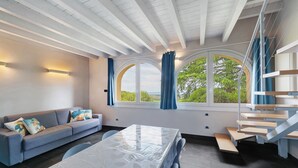 A modern interior with a sofa, table, staircase, and large windows.