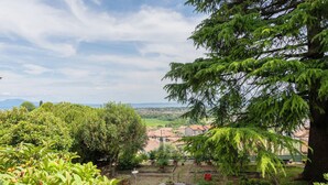 A garden with a stone table and benches, surrounded by trees and a view of a village.