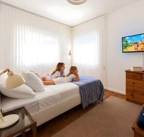 Un dormitorio con cama, televisor, lámpara y cómoda.