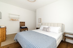 Una camera da letto con un letto, una cassettiera in legno, un comodino e una mensola a parete con appendini.