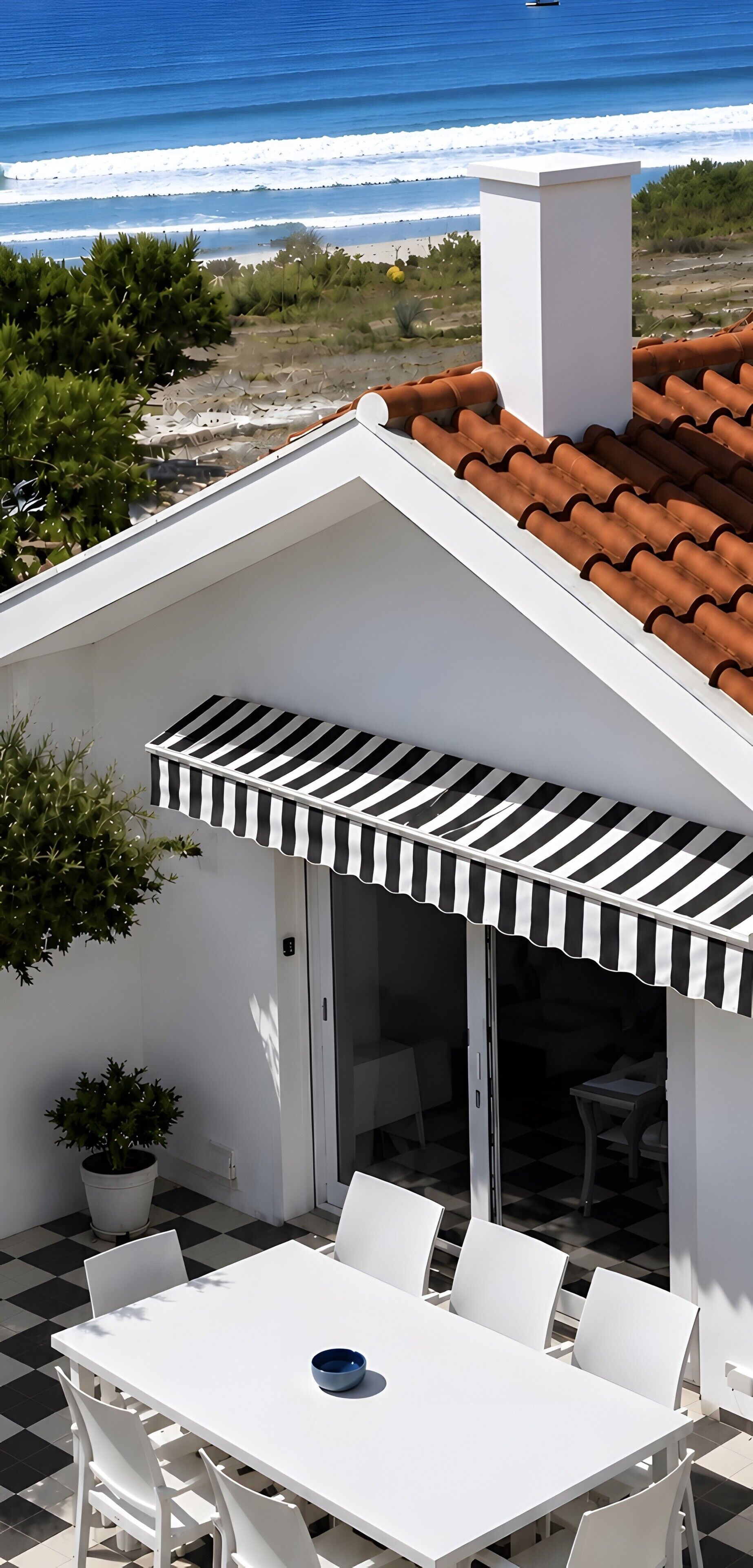 A white building with a tiled roof, a black and white striped awning, and a patio with a table and chairs.