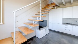 Eine moderne Küche mit weißen Schränken, einem eingebauten Herd und einer Holztreppe mit integrierten Regalen.