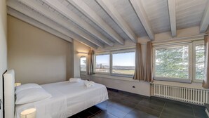 Ein Schlafzimmer mit einem Bett, einer Nachttischlampe, großen Fenstern und Blick ins Freie.