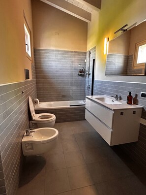 Ein modernes Badezimmer mit Badewanne, Toilette, Bidet und einem Waschtisch mit Spiegel.