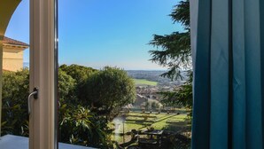 Blick aus einem Fenster auf einen gepflegten Garten mit Rasen, Bäumen und einer in der Ferne liegenden Stadt.