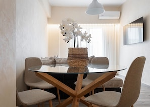 A modern dining area with a glass table, woven centerpiece, and matching chairs. - Glyfada Lux Olive Suites - Pathos (Glyfada)