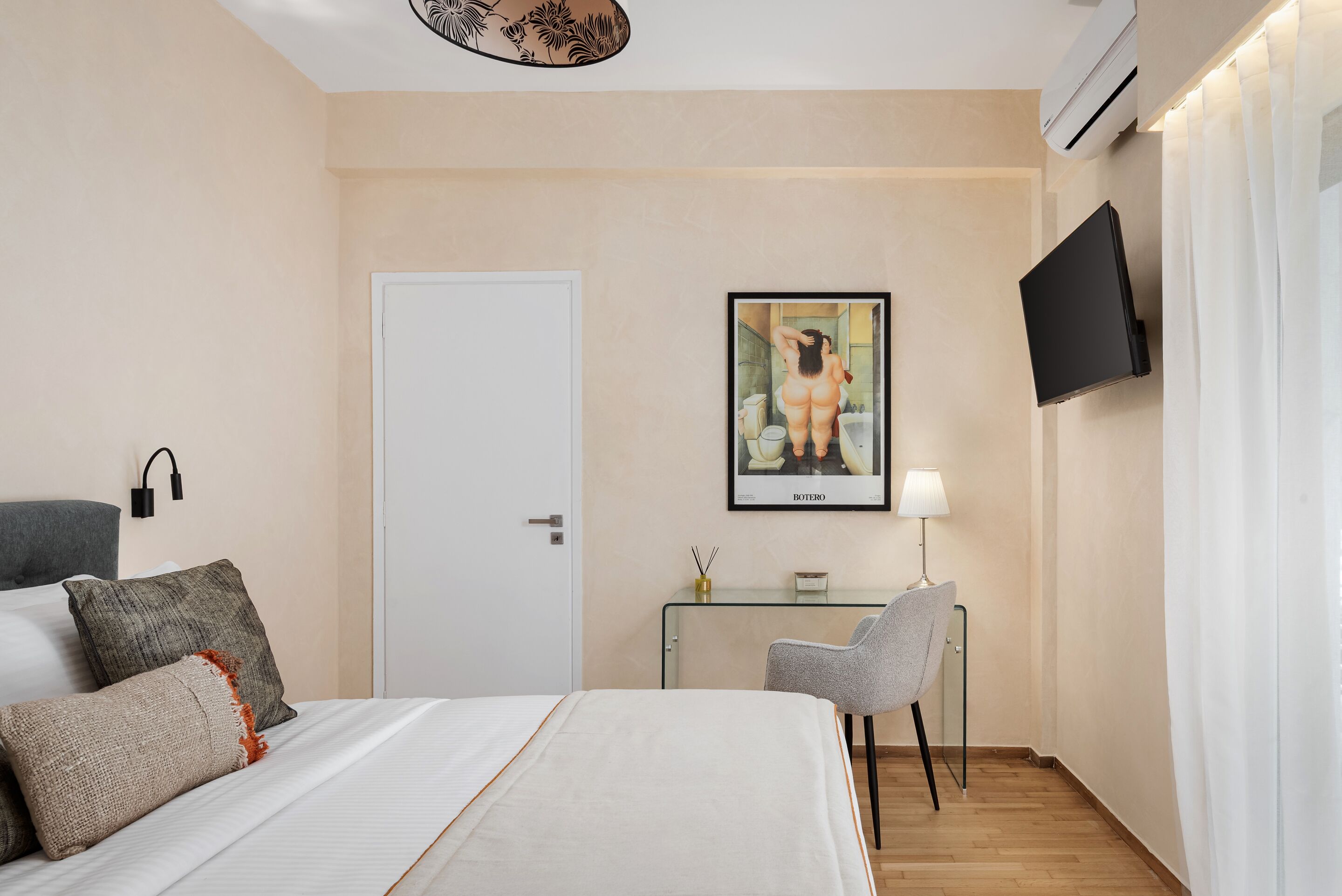 Ett hotellrum med en säng, ett skrivbord, en stol, en tv och en inramad tavla på väggen.