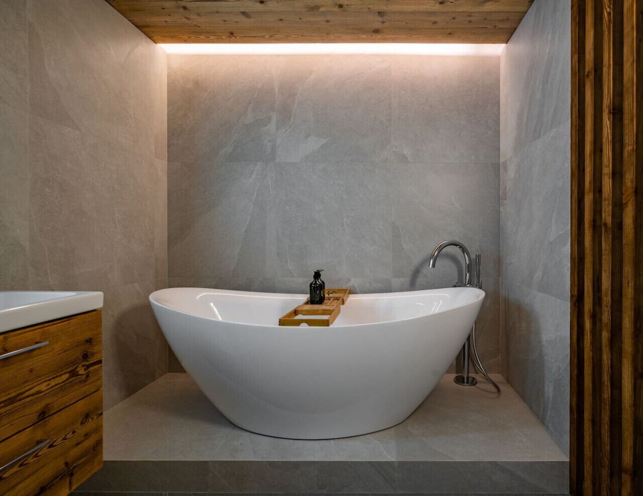Un baño moderno con una bañera independiente, muebles de madera y pared con azulejos.