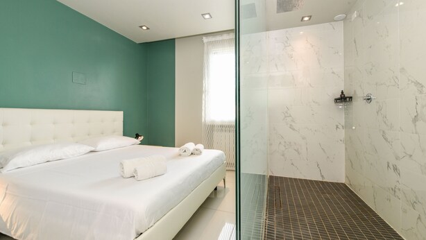 Un dormitorio con una cama grande, cabina de ducha de vidrio y ventana con cortinas.