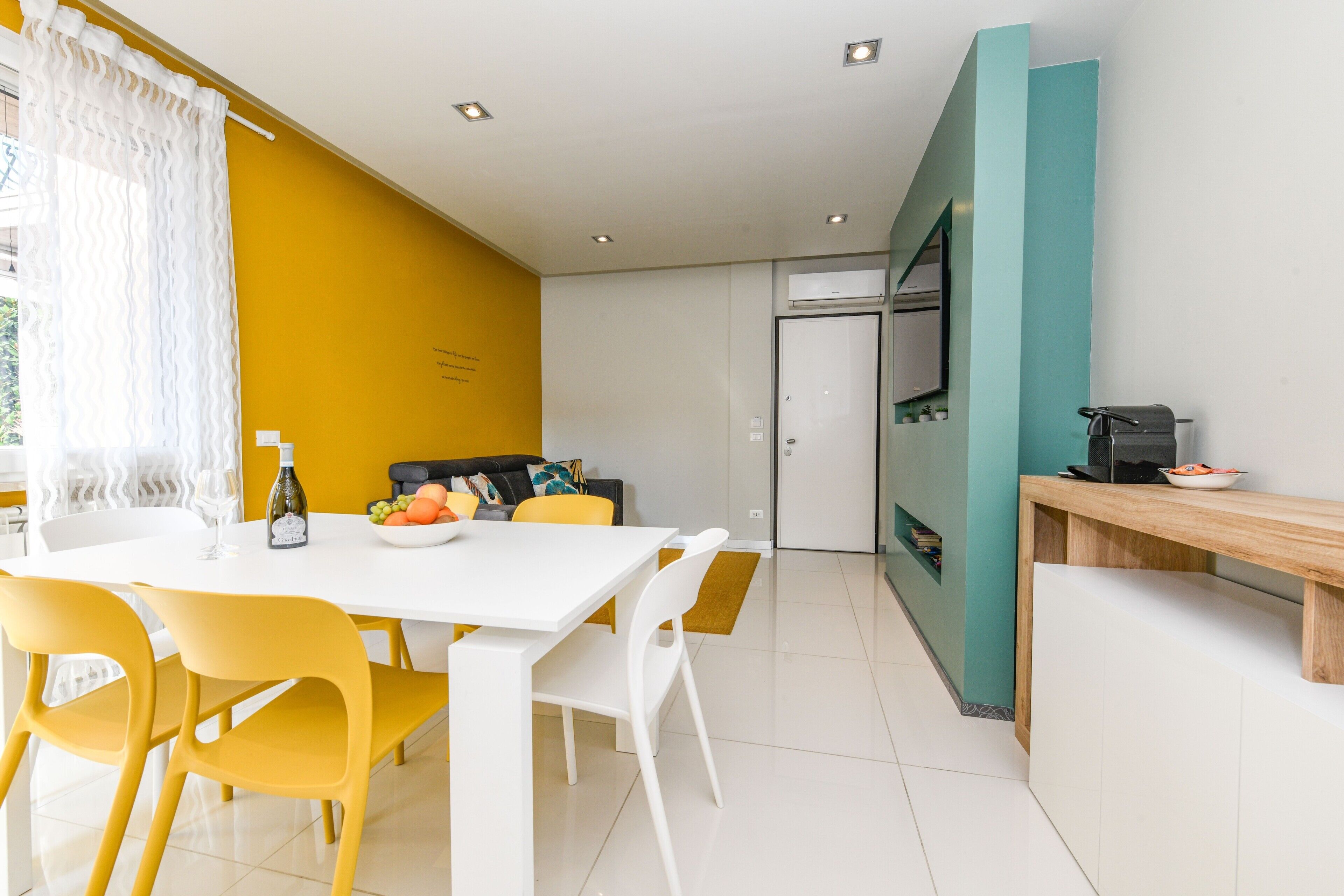 Una cocina moderna con una mesa blanca, sillas amarillas y una pared de acento color aguamarina.