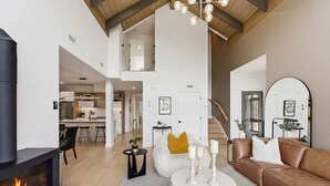A spacious living area with a fireplace, a brown leather sofa, a round coffee table, and a staircase leading to an upper level. - Mountain Luxe | 4BDR Verbier | Jacuzzi & Sauna (Mont-Tremblant)