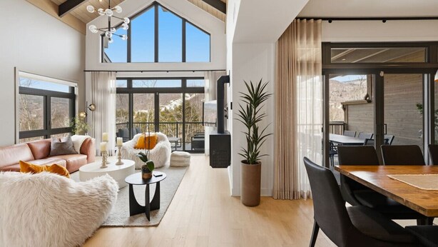 A spacious living area with a high ceiling, large windows, a dining area, and a view of the outdoors. - Mountain Luxe | 4BDR Verbier | Jacuzzi & Sauna (Mont-Tremblant)