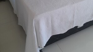 A large bed with a white bedspread, a heart-shaped pillow, and folded towels.