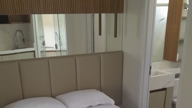 A neatly made bed with a white bedspread and pillows, a folded towel on the bed, and a wooden headboard.