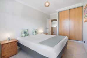 A bedroom with a bed, bedside table, lamp, and wardrobe. - Holiday Home 'Edificio Nora - Quarteira' with Balcony, Wi-Fi and Air Conditioning (Quarteira)