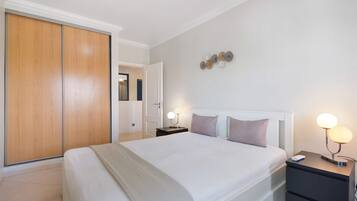 Une chambre avec un grand lit, une armoire, une table de chevet avec une lampe et un luminaire fixé au mur.
