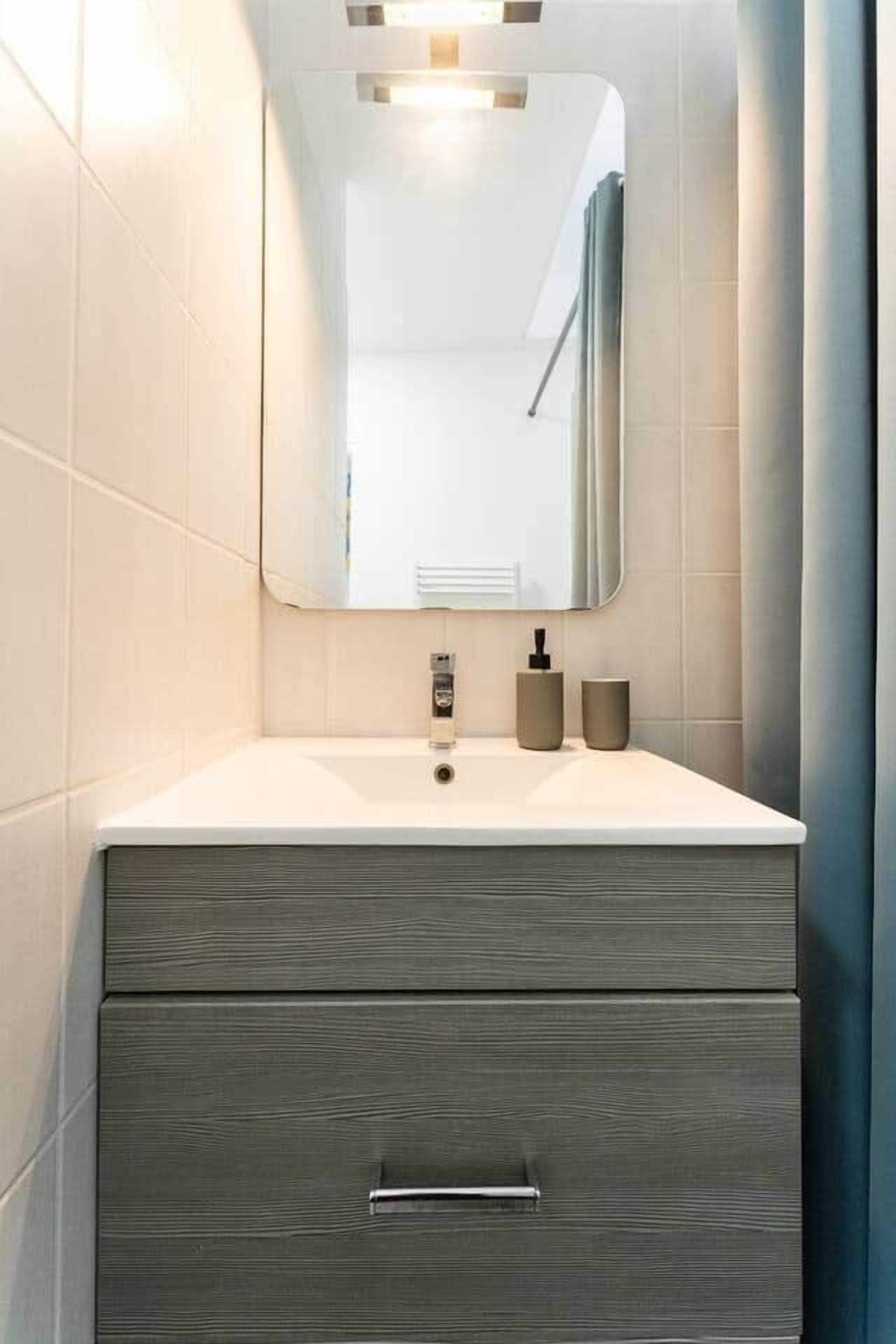 A bathroom with a white vanity, a mirror, and a grey cabinet.