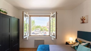 A bedroom with a large window, a bed, a bedside table with a lamp, and a dark wardrobe. - Bright T2 in the heart of Fontenilles (Fontenilles)