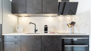 A modern kitchen with dark cabinets, a white countertop, a black faucet, a coffee maker, and a range hood. - Bright T2 in the heart of Fontenilles (Fontenilles)