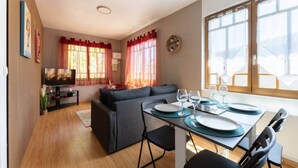 A modern living room with a sofa, dining table set for two, and a TV. - Bright T2 in the heart of Fontenilles (Fontenilles)