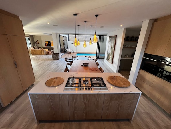 A modern kitchen with a central island, wooden cabinets, and pendant lighting.