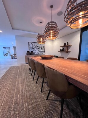 A modern dining area with a long wooden table, multiple chairs, and pendant lighting.