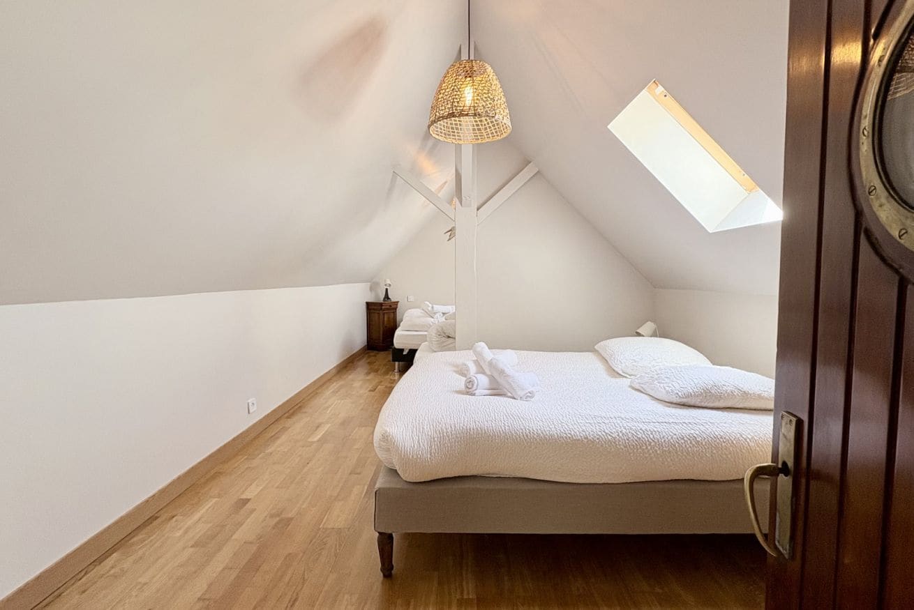 A bedroom with a bed, a hanging light fixture, a small bedside table, and a window.
