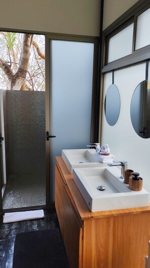A modern bathroom with a wooden vanity, two sinks, a mirror, and a glass door leading to a shower area. - Ocean View Boutique Retreat 4 with big Pool,BBQ,Blue Zone, Bioluminescence, Curu (Paquera)
