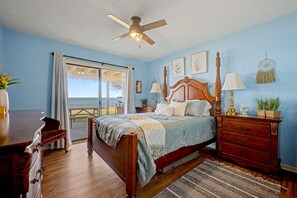 A bedroom with a bed, a nightstand, a dresser, a ceiling fan, and a view of the outdoors.