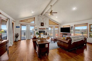 A spacious living room with a fireplace, leather sofas, a television, and large windows offering a view.