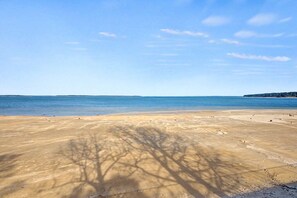 Une plage de sable fin, avec une eau cristalline et une ligne d’arbres qui se dessine à l’horizon.