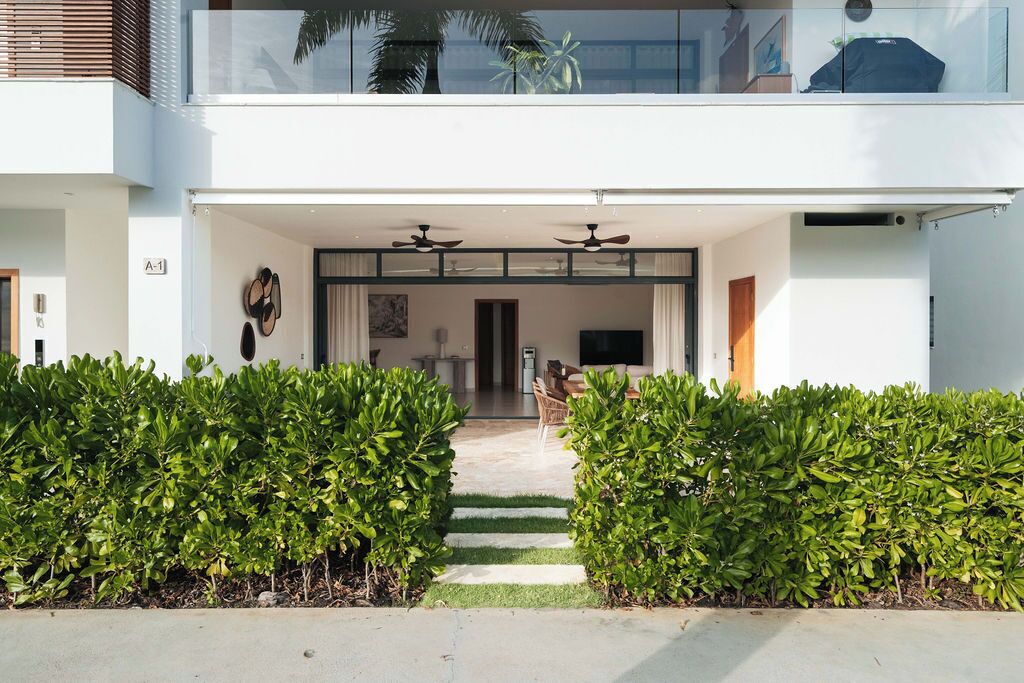 A modern two-story house with a covered entrance, a flat roof, and a balcony with a glass railing.