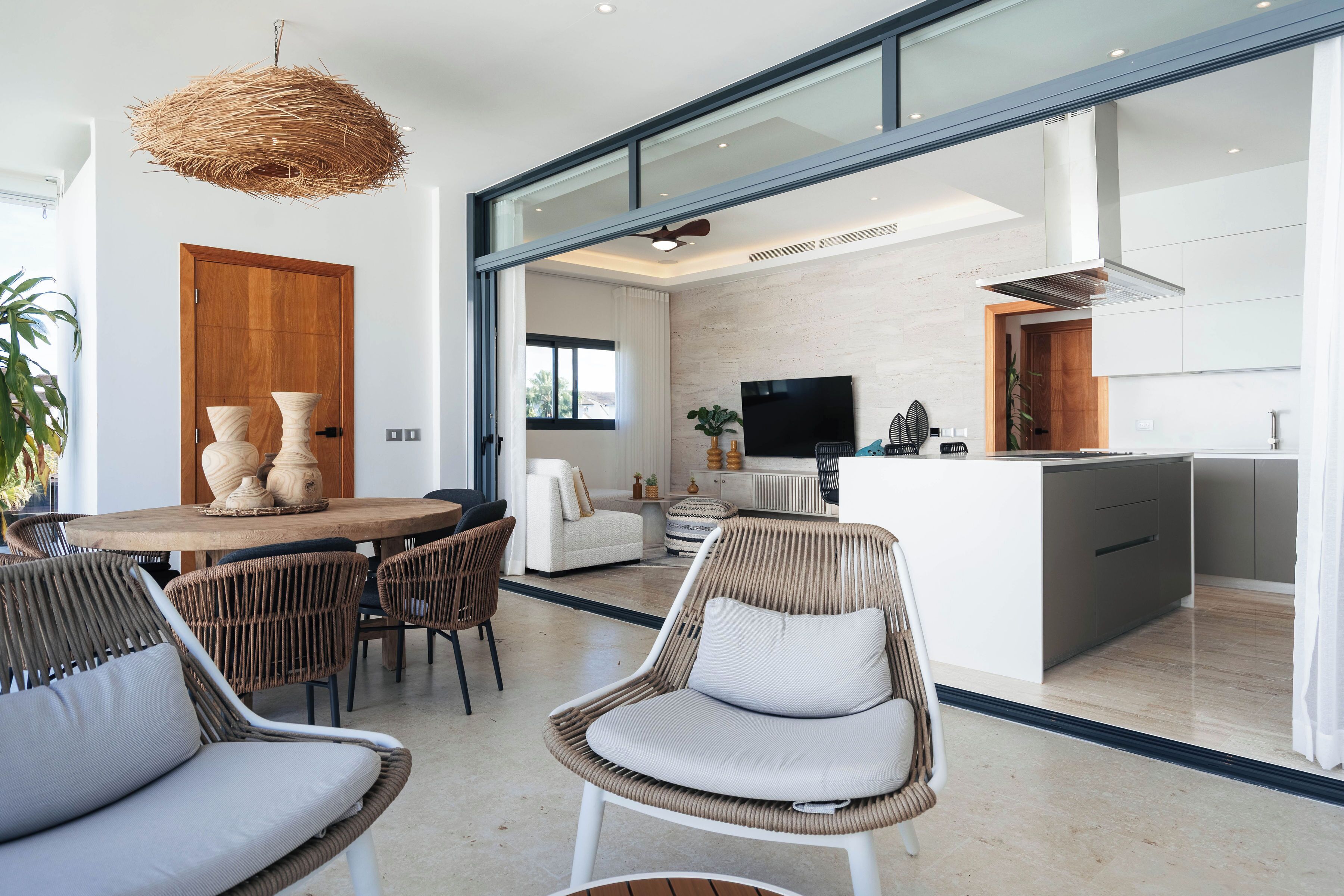 A modern interior with a dining area, wicker chairs, a wooden dining table, and a kitchen with a TV.