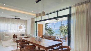 A modern living room with a wooden dining table, white sofas, and a large window with a view of the ocean. - Sol de Arena Beachfront Condos (Las Terrenas)