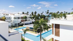 A modern resort with a pool area, palm trees, and white buildings. - Sol de Arena Beachfront Condos (Las Terrenas)