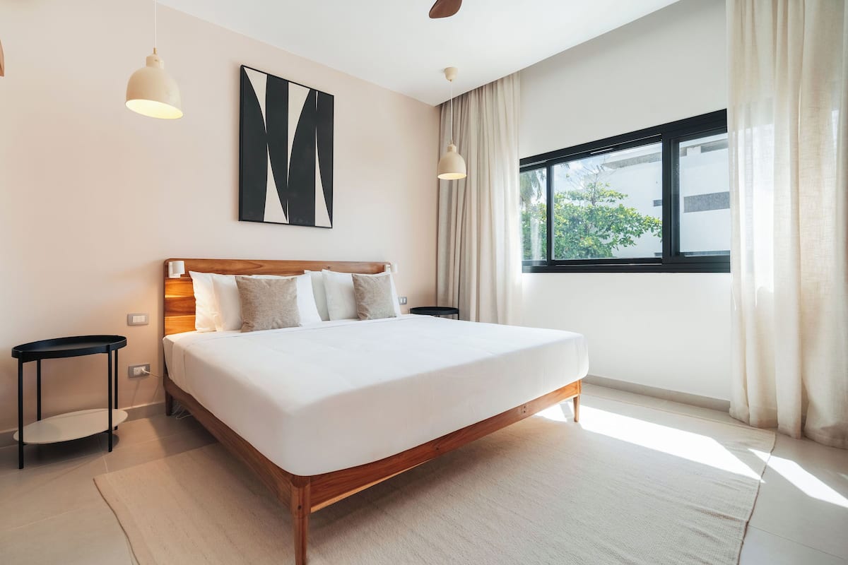 A modern bedroom with a large bed, bedside tables, a window with curtains, and a ceiling fan.