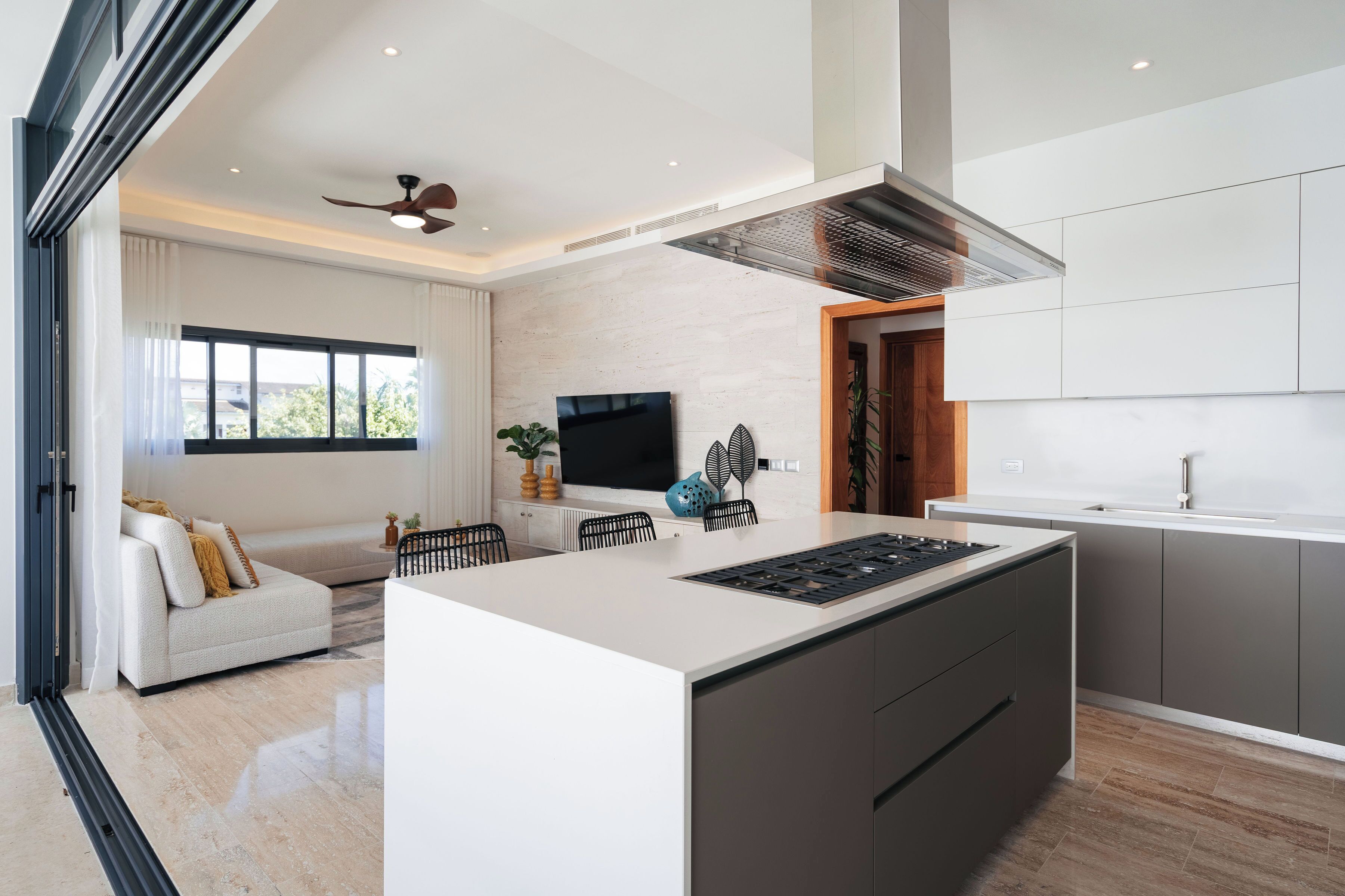 Una cocina moderna con una isla central, un área de comedor con sofá y un amplio ventanal que proporciona luz natural.