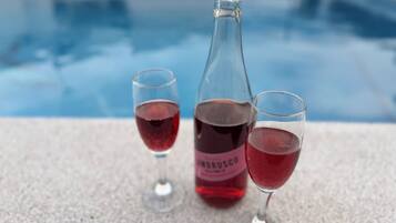 A poolside setting with a bottle and two glasses of red beverage.