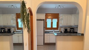 A kitchen with white cabinets, a refrigerator, and a window with lace curtains.