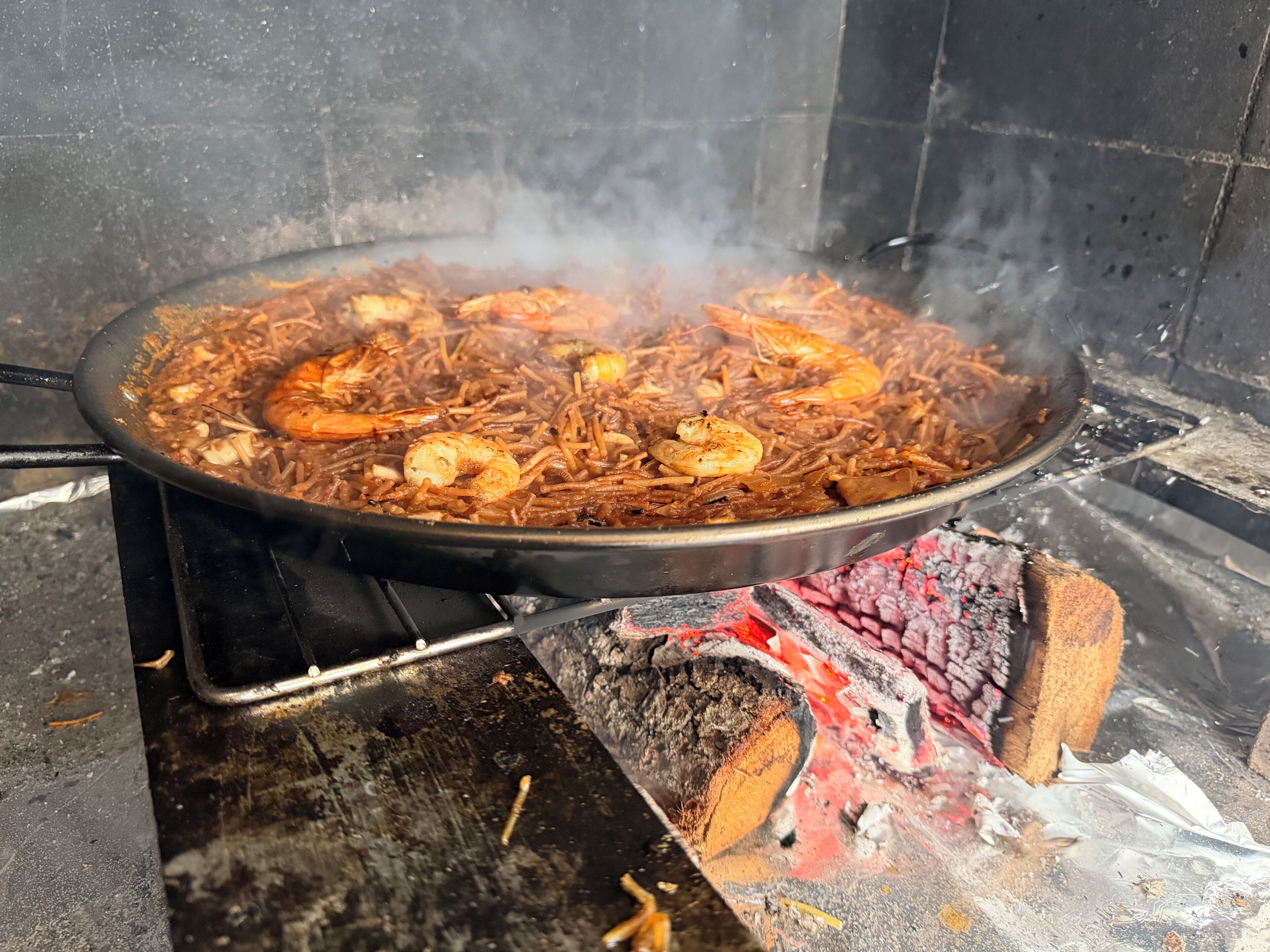 A large pan filled with a seafood dish over an open flame.